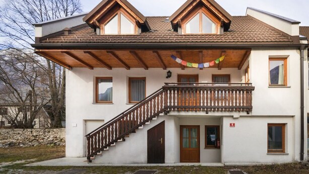 A two-story building with a balcony, wooden staircase, and a tiled roof.