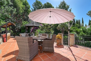 Une terrasse extérieure aménagée avec des meubles en osier, une table et un grand parasol.