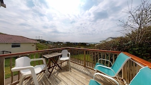 A wooden deck with white plastic chairs and a table, overlooking a residential area with houses and a clear sky.