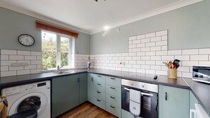 A modern kitchen with a washing machine, a sink, and a window with blinds.