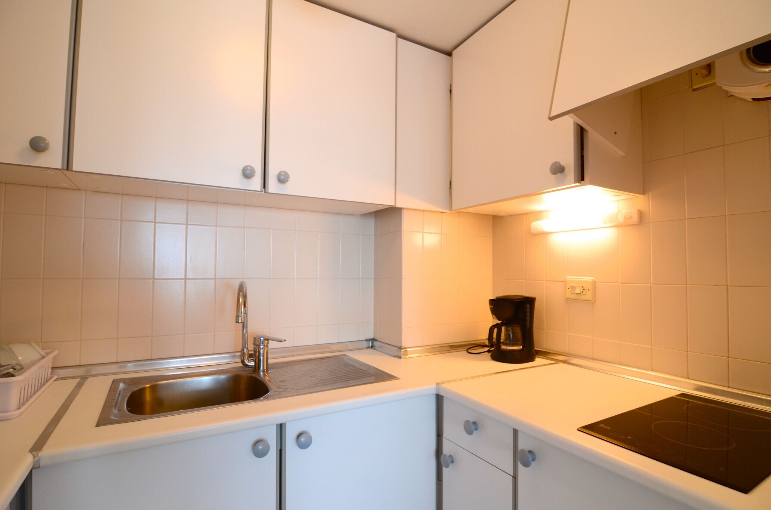 A modern kitchen with white cabinets, a stainless steel sink, and a black induction cooktop.