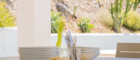 Une table à manger avec une pile d’assiettes blanches, une tasse en verre transparent et des couverts en métal.