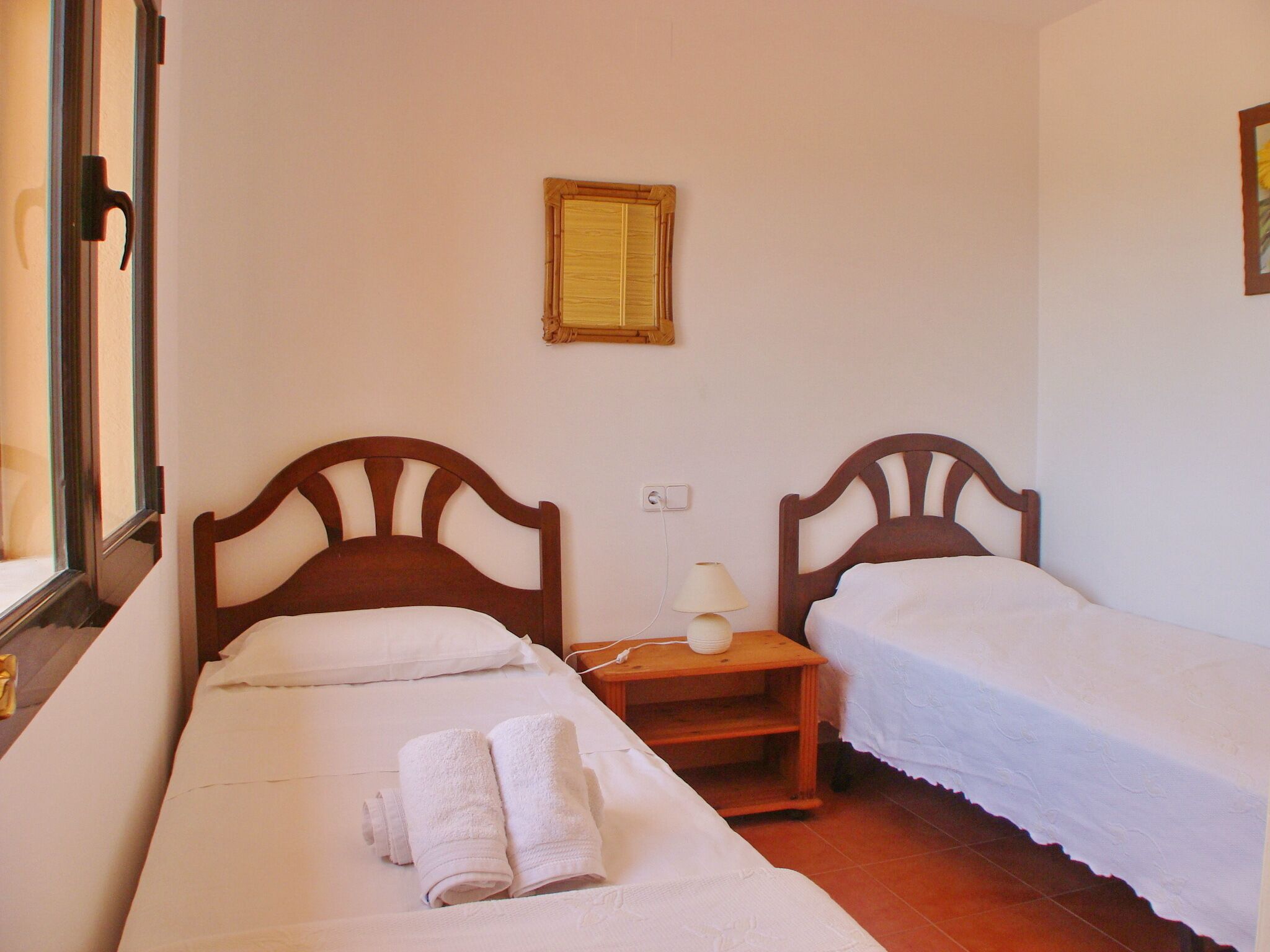 Una habitación con dos camas individuales, una mesita de noche con lámpara y un cuadro en la pared.