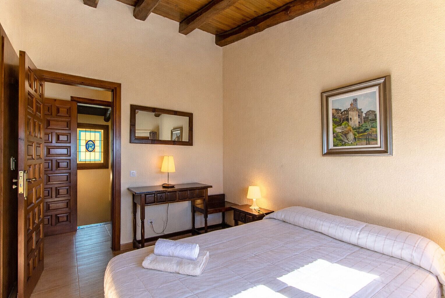 A hotel room with a bed, desk, and chair, a mirror, and a painting on the wall.