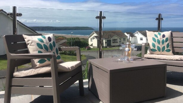 An outdoor seating area with a view of the sea and houses in the background. - 2 Bed in Woolacombe (oc-high77) (Woolacombe)