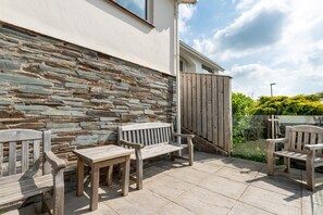 A patio area with stone walls, wooden benches, and a wooden fence. - 2 Bed in Woolacombe (oc-high77) (Woolacombe)