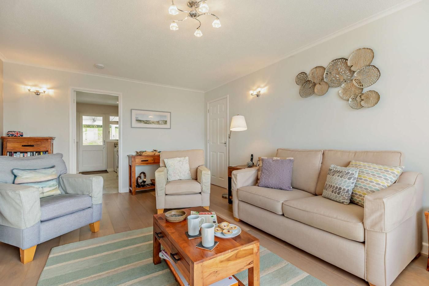 A living room with a sofa, armchairs, a coffee table, and a lamp. There is a door leading to another room.