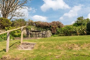 A garden with a wooden pergola, a stone wall, and a seating area with metal chairs. - 2 Bed in Woolacombe (oc-high77) (Woolacombe)