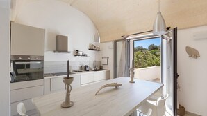 Una cocina moderna con armarios blancos, un ventanal y vista a zonas verdes.