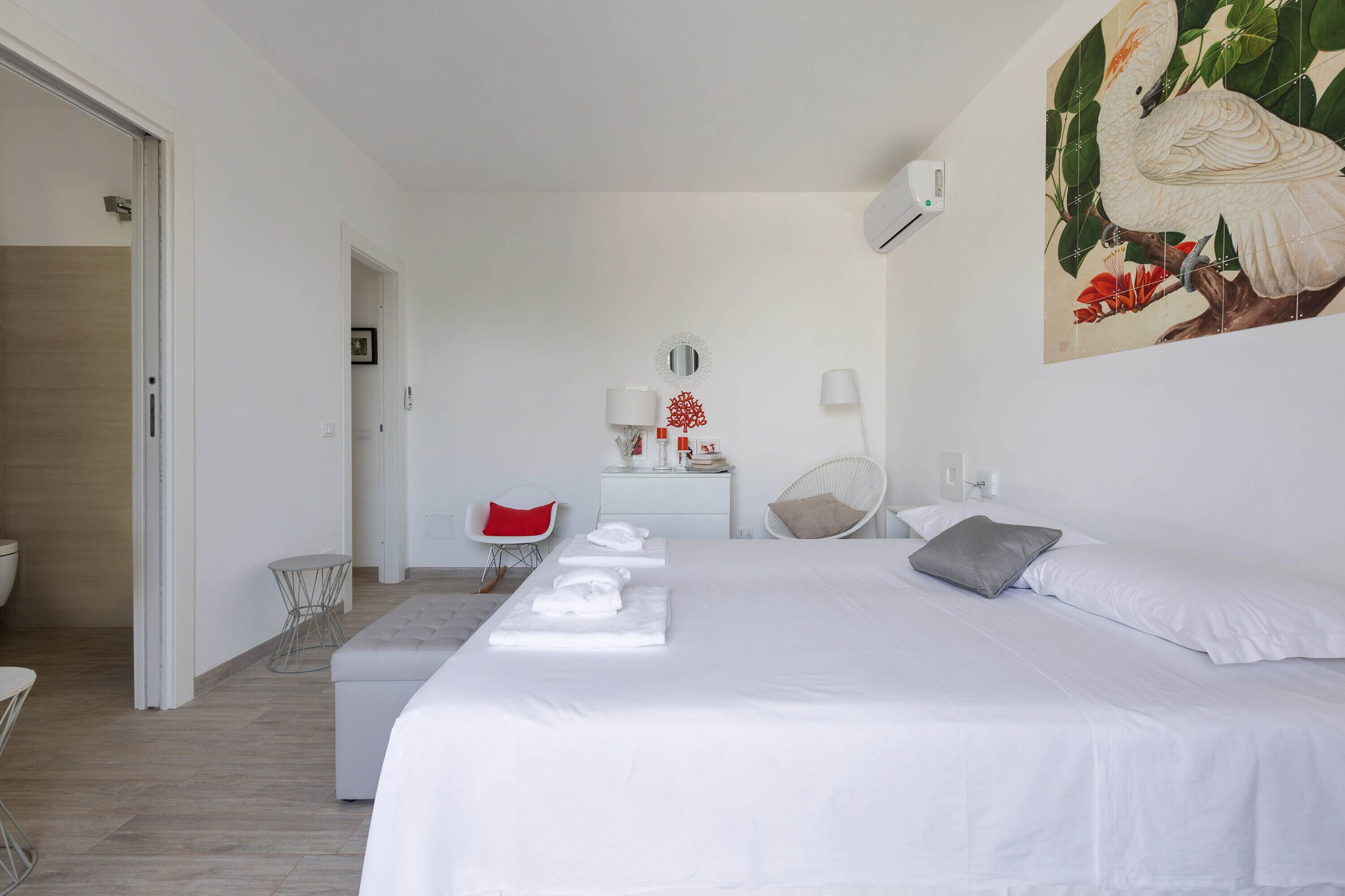 Une chambre d’hôtel avec un grand lit, une petite table, une chaise, une table de chevet avec une lampe et un climatiseur fixé au mur.