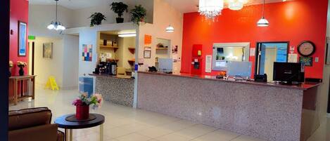 A reception area with a red wall, a counter with computers, a clock, and a chandelier.