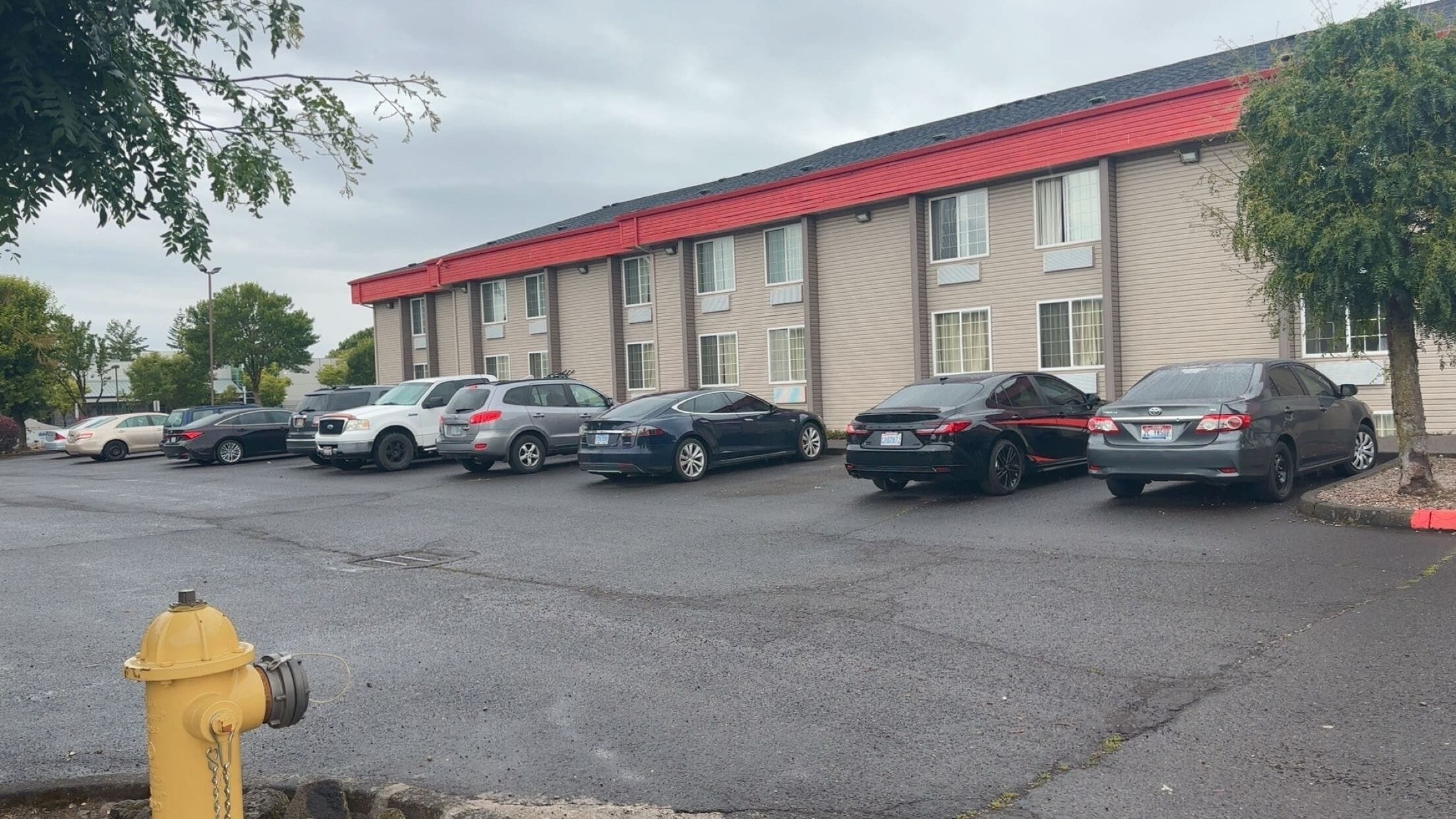 A parking lot with several cars parked in front of a building with a red roof and beige siding.