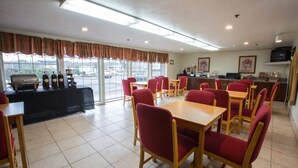 Un espace repas avec des chaises et des tables rouges, un coin barbecue et une vue sur le parking grâce à de grandes fenêtres.