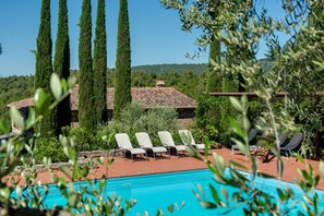 A pool area with lounge chairs, a tiled roof, and tall cypress trees. - Tuscany Villa with Breathtaking View at Dotholiday (Civitella in Val di Chiana)