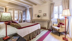 Et hotelværelse med seng, skrivebord, stol, lampe, vindue og radiator.
