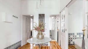 A hallway with a round table and a vase of flowers, wooden flooring, and white walls with patterned borders.
