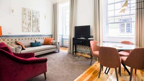 A living room with a sofa, a red armchair, a TV, and a dining table with chairs.