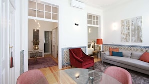 A spacious living room with a glass coffee table, a red armchair, a grey sofa, and a patterned wall.
