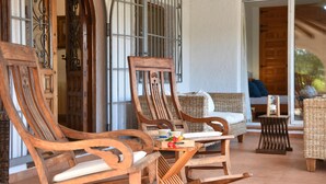 A wooden rocking chair and a wicker sofa on a tiled patio with a view of a wooden door and a metal gate. - Villa in Javea, on the Costa Blanca, Spain with private pool for 6 persons (Javea)