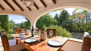 An outdoor dining area with a wooden table set for four, surrounded by chairs, with a view of greenery and trees. - Villa in Javea, on the Costa Blanca, Spain with private pool for 6 persons (Javea)