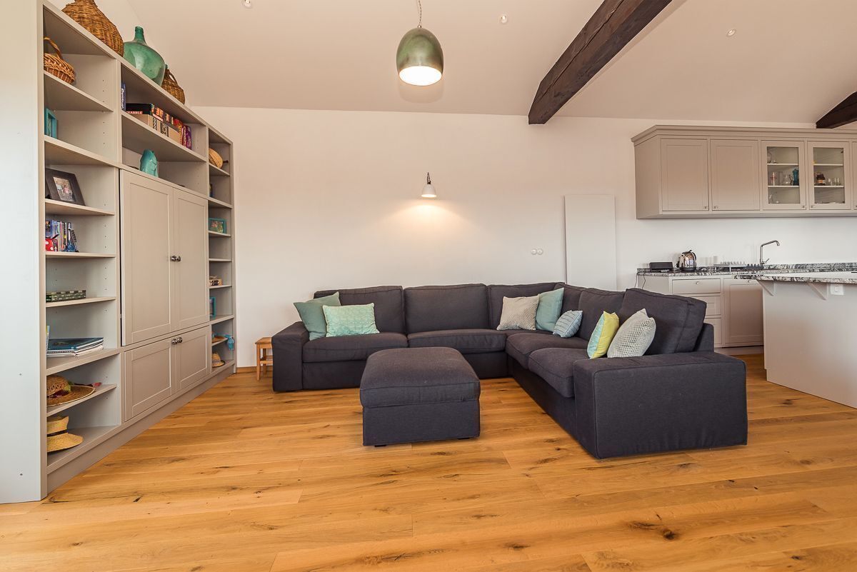 A modern living room with a sectional sofa, ottoman, and a bookshelf filled with decorative items.