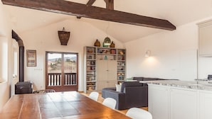 Een ruime woonkamer met een houten eettafel, een grijze bank en een keuken met witte kasten.