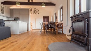Een ruime woonkamer met houten vloer, een eettafel met stoelen, een bank en een open haard.