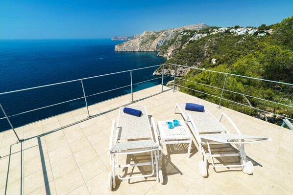 A terrace with two sun loungers, a table, and a drink tray, overlooking a coastal landscape with cliffs and the sea. - Villa Bombon - Javea, Costa Blanca (Javea)