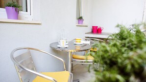 Eine kleine Außenveranda mit einem runden Tisch, zwei Stühlen, einem Blumentopf und einem Fenster mit Blick.