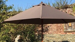 En udendørs terrasse med et bord, stole og en stor parasol, med en stenvæg i baggrunden.