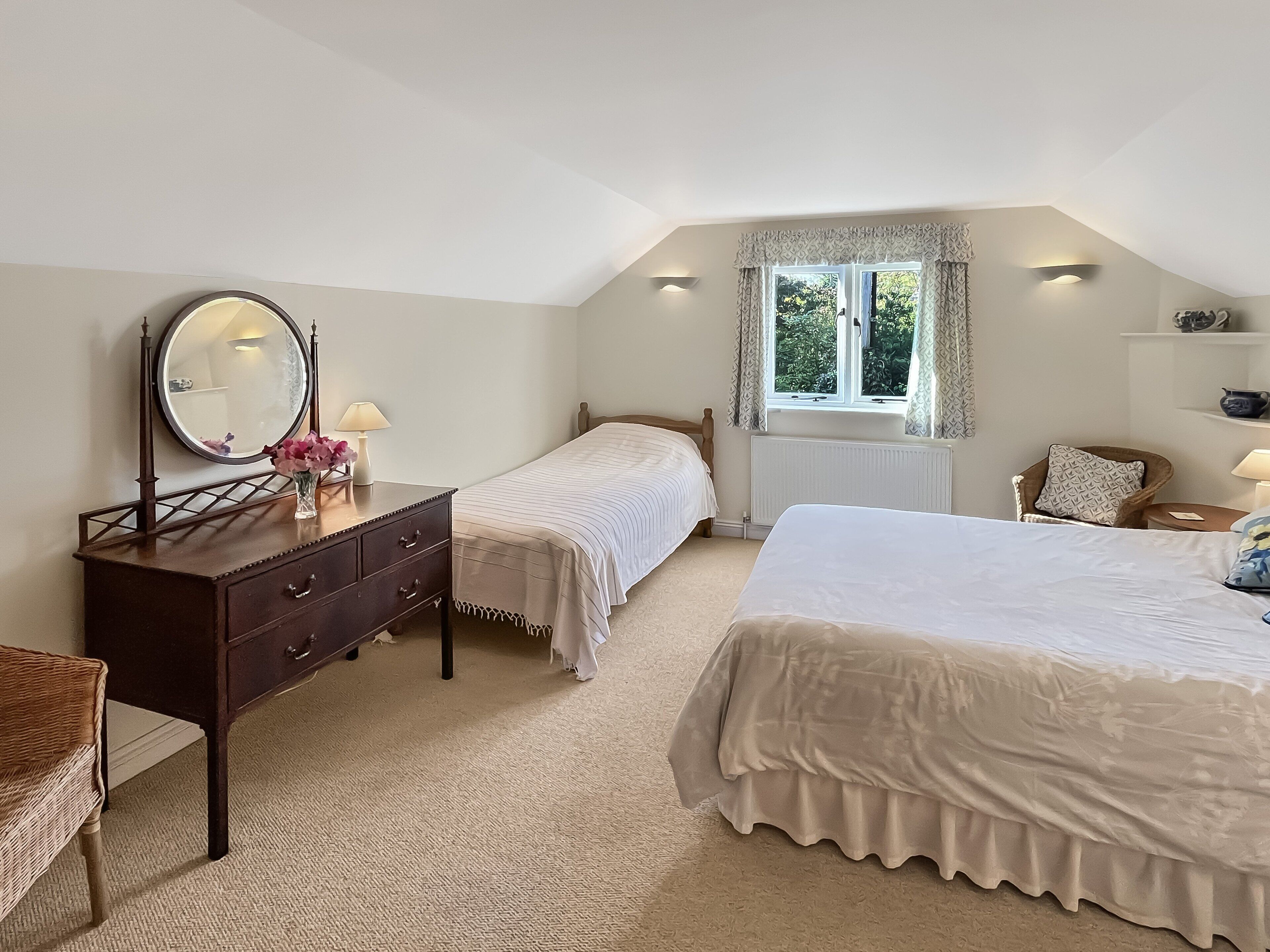 Een slaapkamer met twee bedden, een kaptafel, een spiegel en een raam met gordijnen.
