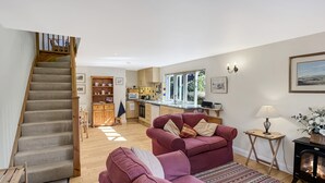 A living room with a staircase, a kitchen, and a fireplace. - Forge Cottage, Wootton Courtenay (Wootton Courtenay)