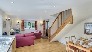 A spacious living area with a wooden staircase, a dining table set with white dishes, and a red sofa. - Forge Cottage, Wootton Courtenay (Wootton Courtenay)