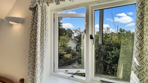 A room with a large window, a bed with a headboard, and a wall-mounted light fixture. - Forge Cottage, Wootton Courtenay (Wootton Courtenay)