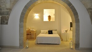 Une chambre à coucher avec un lit, un bureau et une chaise. Il y a une fenêtre et un vase est posé sur le mur.
