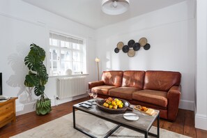A living room with a brown leather sofa, a coffee table with fruit and cheese, a green plant, and a white radiator.
