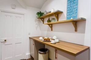 A small kitchenette with a wooden countertop, a trash bin, and a white door.