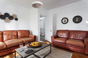A living room with two brown leather sofas, a coffee table with a fruit bowl and wine glasses, and a white ceiling light.