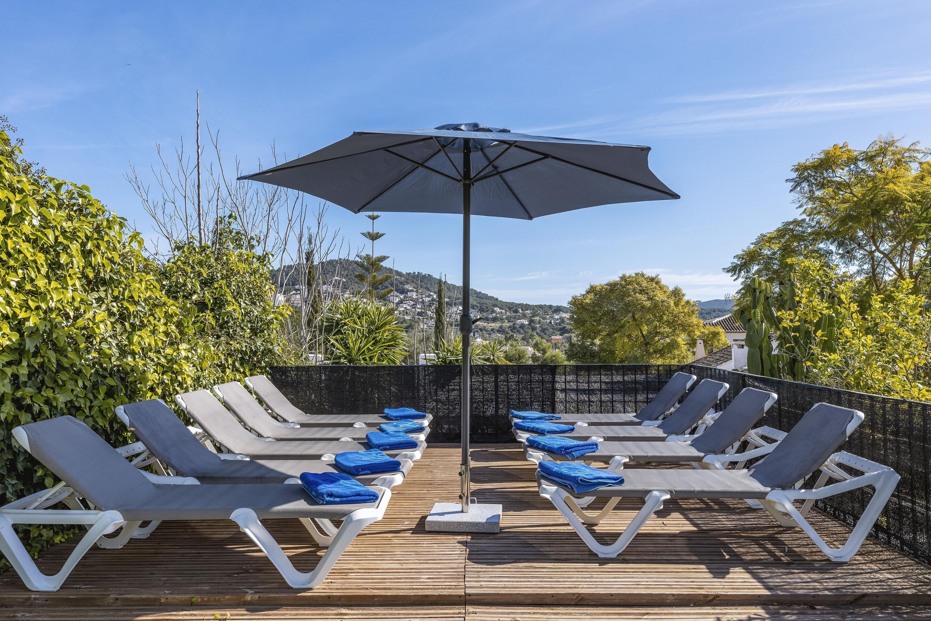 A deck with sun loungers and a large umbrella, overlooking a scenic landscape.