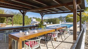 En udendørs terrasse med et træbord og stole, en pool og udsigt over det omkringliggende landskab.