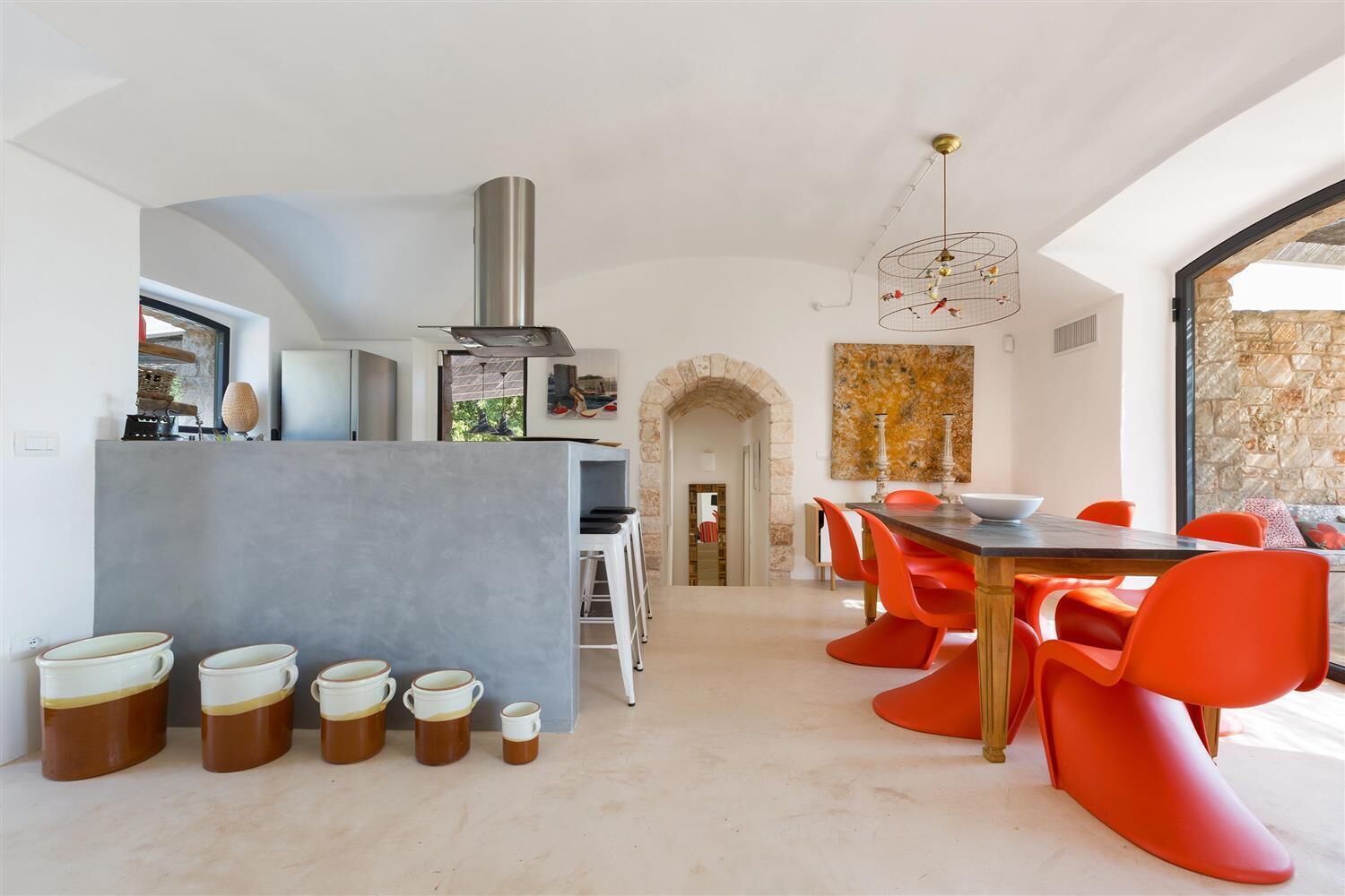 A modern kitchen with a central island, a dining area with orange chairs, and a stone wall.