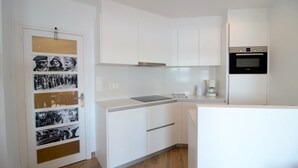 Una cocina moderna con armarios blancos, horno empotrado y cafetera.