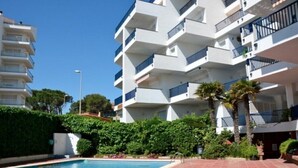 Un moderno edificio residencial de varios pisos con balcones, piscina y abundante vegetación.