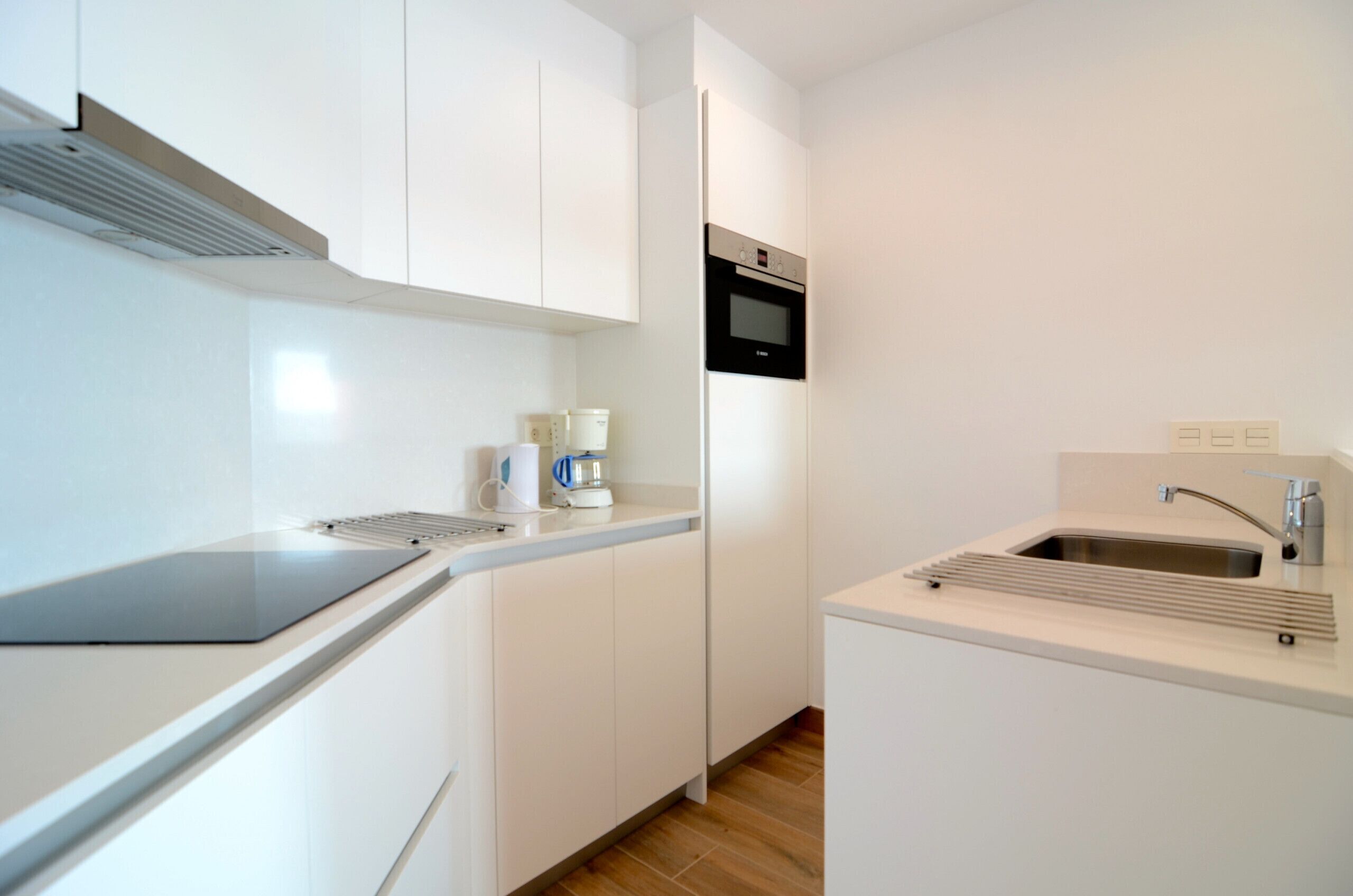 A modern kitchen with white cabinetry, a built-in oven, a coffee maker, and a sink with a faucet.