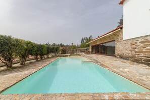 Une piscine rectangulaire bordée de pierres, entourée d’un mur de pierres et d’une terrasse en bois.