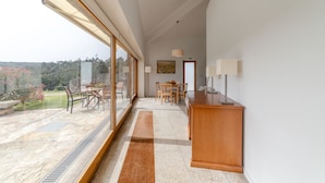 A spacious room with a large sliding glass door leading to a patio, a wooden dining table, and a small kitchenette area. - Nature, the Douro, and Porto in an Exclusive Villa (Gondomar)