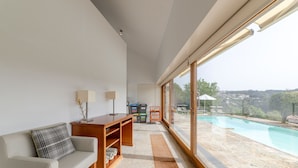 A modern living room with a sofa, a wooden side table, and a large window overlooking a swimming pool. - Nature, the Douro, and Porto in an Exclusive Villa (Gondomar)