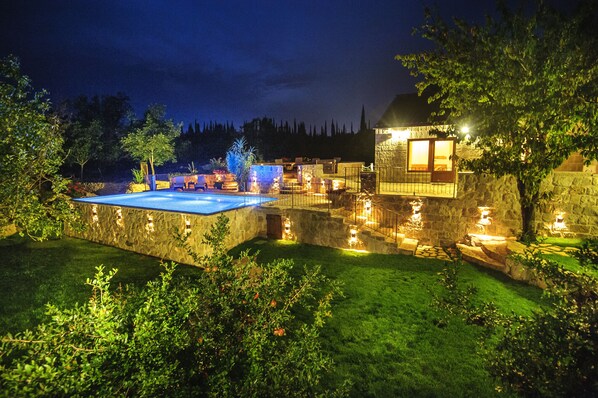 A stone pool surrounded by a stone wall, with a small building and a tree in the background.