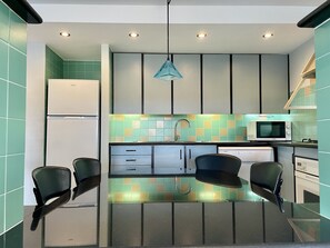 A modern kitchen with a refrigerator, microwave, sink, and two chairs.