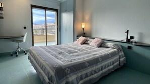 Ein Schlafzimmer mit Bett, Schreibtisch, Stuhl, Nachttisch und einem Fenster mit Blick.